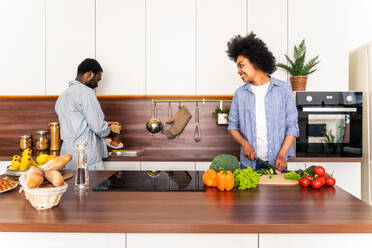 Schönes afroamerikanisches Paar, das zu Hause kocht - Schönes und fröhliches schwarzes Paar, das gemeinsam in der Küche das Abendessen vorbereitet - DMDF07133
