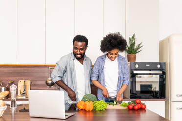 Schönes afroamerikanisches Paar, das zu Hause kocht - Schönes und fröhliches schwarzes Paar, das gemeinsam in der Küche das Abendessen vorbereitet - DMDF07134