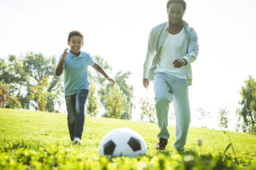 Beautiful happy african american family bonding at the park - Black family having fun outdoors, father and son playing football - DMDF07211