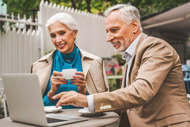 Beautiful senior couple dating outdoors - Mature couple with laptop computer sitting in a bar restaurant, concepts about elderly, lifestyle and technology - DMDF07303