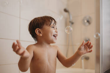 Cheerful boy playing with soap bubbles in bathtub - ANAF02214