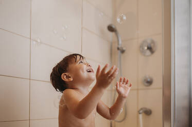 Happy boy playing with soap bubbles in bathroom - ANAF02215