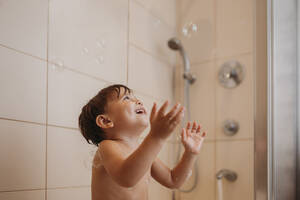 Glücklicher Junge spielt mit Seifenblasen im Badezimmer - ANAF02215