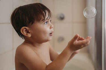 Boy catching soap bubble in bathroom - ANAF02217