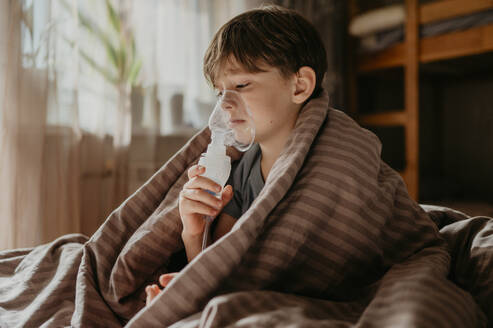 Elementary boy inhaling through nebulizer at home - ANAF02222