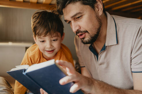 Vater liest seinem Sohn im Schlafzimmer zu Hause ein Buch vor - ANAF02227