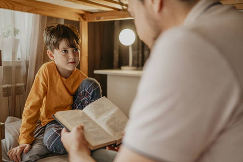 Father reading book to son in bunk bed at home - ANAF02228