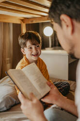 Father reading book to happy son in bunk bed at home - ANAF02229