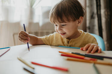 Smiling boy drawing with colored pencil at home - ANAF02231