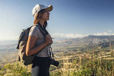 Junge Frau mit Rucksack und Kamera beim Wandern an einem sonnigen Tag - JSRF02653