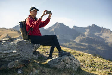 Junge Frau sitzt auf einem Felsen und fotografiert mit ihrem Smartphone - JSRF02667