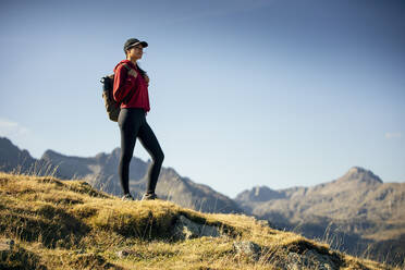 Junge Frau mit Rucksack beim Wandern in den Bergen an einem sonnigen Tag - JSRF02669
