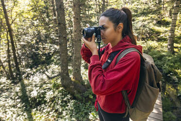 Junge Frau fotografiert mit Kamera im Wald stehend - JSRF02676