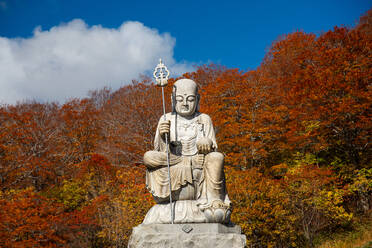 Große Shizo-Statue vor feuerroten Herbstblättern in einem schönen japanischen Tempel, umgeben von Herbstfarben, Osorezan Bodaiji-Tempel, Mutsu, Präfektur Aomori, Honshu, Japan, Asien - RHPLF28226