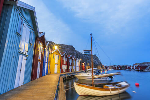 Colorful fishing huts with wooden boat moored at the jetty at dusk, Smogen, Bohuslan, Vastra Gotaland, West Sweden, Sweden, Scandinavia, Europe - RHPLF28669