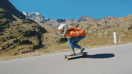 Cinematic downhill longboard session. Young woman skateboarding and making tricks between the curves on a mountain pass. Concept about extreme sports and people - DMDF07451