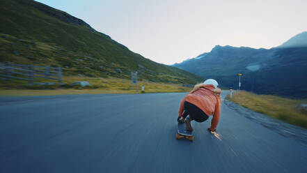 Cinematic downhill longboard session. Young woman skateboarding and making tricks between the curves on a mountain pass. Concept about extreme sports and people - DMDF07452