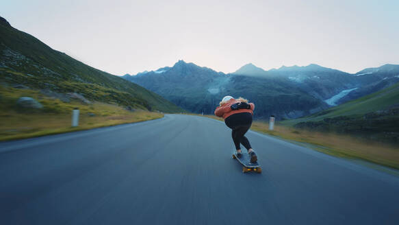 Cinematic downhill longboard session. Young woman skateboarding and making tricks between the curves on a mountain pass. Concept about extreme sports and people - DMDF07454