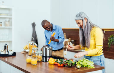 Cinematic image of a multiethnic senior couple preparing food in the kitchen. Indoors Lifestyle moments at home. Concept about seniority and relationships - DMDF07588