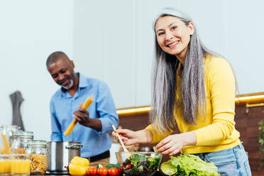 Cinematic image of a multiethnic senior couple preparing food in the kitchen. Indoors Lifestyle moments at home. Concept about seniority and relationships - DMDF07589