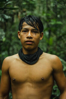 Porträt eines hemdsärmeligen Teenagers eines lokalen Stammes in der Natur des Amazonas-Regenwaldes, der in die Kamera schaut - ADSF48028