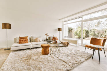 Interior of spacious living room with comfortable sofa and lamps with carpet next to large bright window with white walls at home - ADSF48078