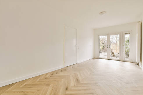 Interior of empty living room with white walls and parquet floors against large bright windows in unfurnished house - ADSF48082