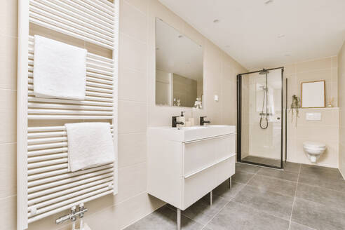 Interior of modern stylish bathroom with shower cabin and toilet bowl in corner and sink with towel rack on tiled wall - ADSF48086