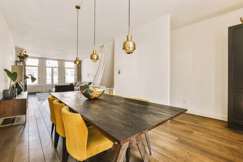 Contemporary dining room with lights hanging over wooden table and yellow chairs arranged on hardwood floor in spacious apartment - ADSF48097