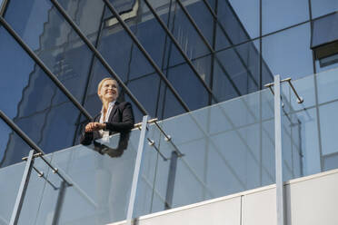 Lächelnde Geschäftsfrau lehnt sich an ein Glasgeländer auf einer Terrasse - OSF02229
