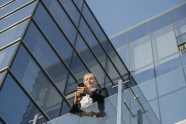 Businesswoman using smart phone leaning on railing - OSF02230