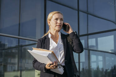 Reife Geschäftsfrau mit Aktenordner im Gespräch auf dem Mobiltelefon - OSF02231