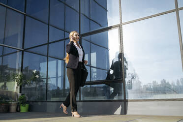 Businesswoman talking over smart phone and walking on terrace - OSF02239