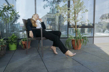 Geschäftsfrau ruht sich auf einem Stuhl auf der Terrasse eines Geschäftszentrums aus - OSF02243
