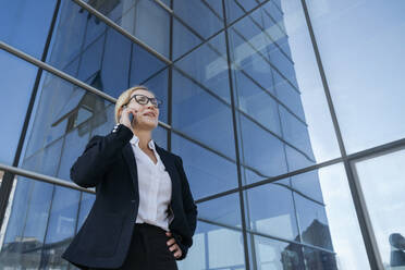 Businesswoman talking on mobile phone by office building - OSF02267