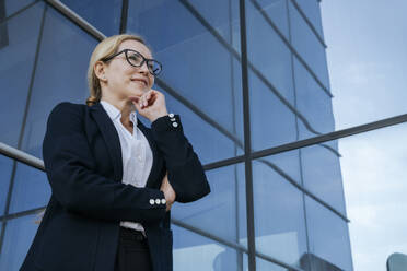 Lächelnde Geschäftsfrau mit Hand am Kinn vor einem Bürogebäude - OSF02270