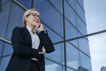 Smiling businesswoman with hand on chin by office building - OSF02270