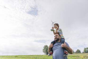 Man carrying son on shoulders with wind turbine model in front of cloudy sky - OSF02279