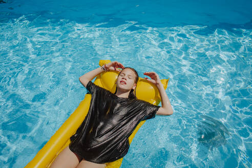 Mädchen mit geschlossenen Augen entspannt sich auf einem Floß im Pool an einem sonnigen Tag - MDOF01578