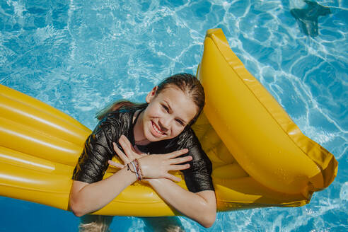 Lächelndes Mädchen lehnt sich auf einer Luftmatratze im Schwimmbad - MDOF01579