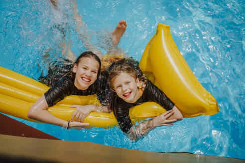 Fröhliche Freunde lehnen sich auf einer Luftmatratze im Schwimmbad - MDOF01582