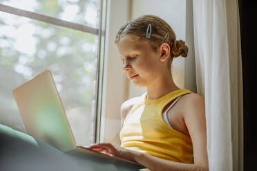 Mädchen benutzt Laptop am Fenster zu Hause - MDOF01593