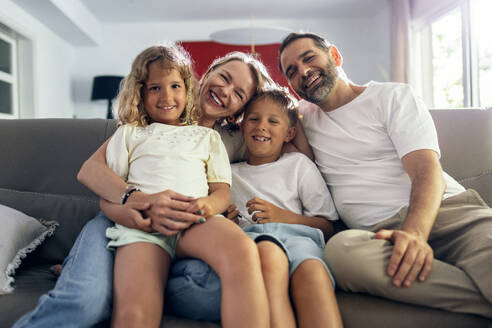 Glückliche Eltern mit Kindern, die zu Hause auf dem Sofa sitzen - JSRF02701