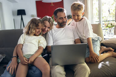 Father sharing laptop with family sitting in living room - JSRF02702