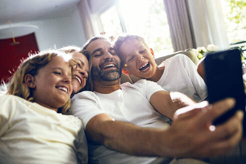 Happy man taking selfie with family on smart phone at home - JSRF02705