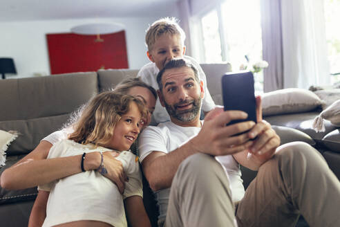 Mature man taking selfie with family on mobile phone at home - JSRF02706