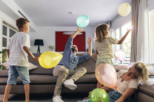 Eine glückliche Familie spielt mit Luftballons im Wohnzimmer - JSRF02717
