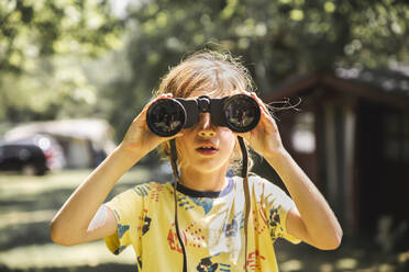 Curious boy looking though binoculars in forest - PCLF00776