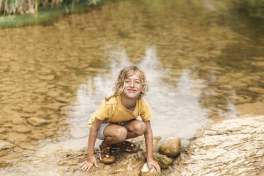 Lächelnder Junge hockt am Fluss - PCLF00790