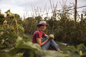 Glückliche Frau hält runde Zucchini im Obstgarten - PCLF00794